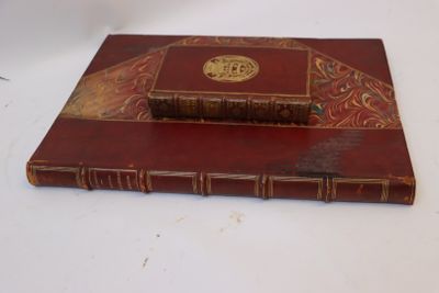 un livre rouge aux tranches dorées posé sur une table blanche