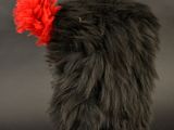 a black sheepskin hat with a red pom pom on top of it