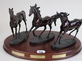 three statues of horses running on a wooden base