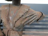a statue of a man sitting on a bench with his hands on his chest