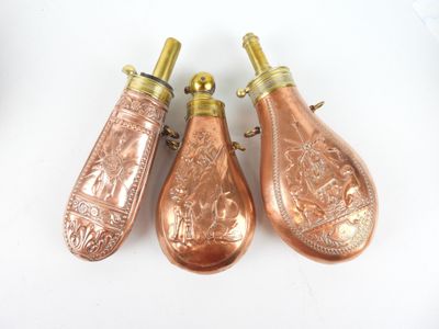 trois briquets anciens en cuivre en forme de bouteille posés sur une surface blanche