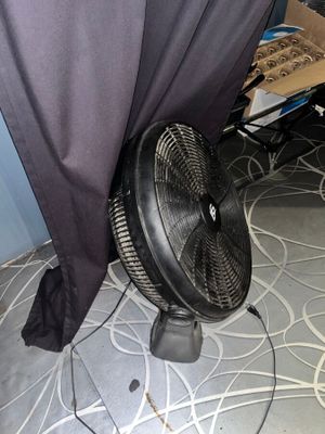 un ventilateur posé par terre devant un rideau