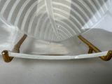 a glass bowl with gold handles on a white table