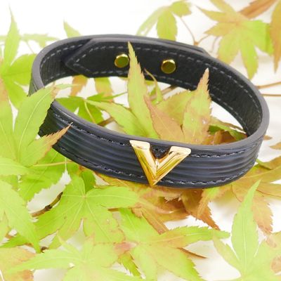 black leather bracelet with gold triangle studs on a pile of leaves