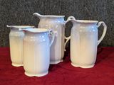 three white pitchers sitting on a red table cloth