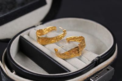 a pair of gold earrings in a case on a black surface