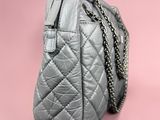a close up of a grey quilted purse on a pink background