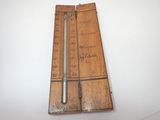 un vieux thermomètre en bois posé sur une table blanche, à côté d'une règle