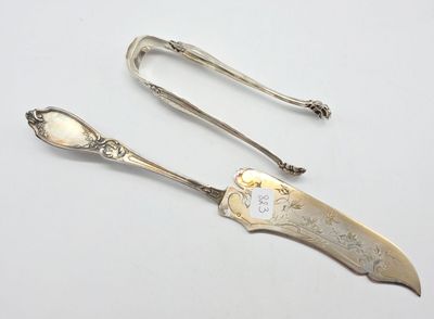 une paire de cuillères et de pinces anciennes en argent posées sur un support blanc