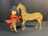 a wooden horse and a man in a red coat standing next to each other