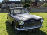 Une vieille voiture noire est garée dans l'herbe devant une maison.