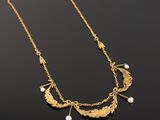 a close up of a gold necklace with pearls on a black surface