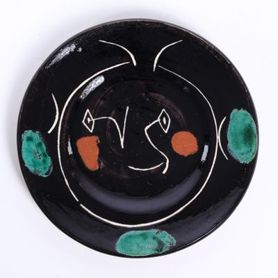une image représentant une assiette noire ornée de motifs verts et orange