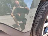 a man squatting on the side of a car with a cell phone in his hand