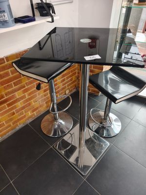 une table noire avec deux tabourets noirs devant un mur de briques