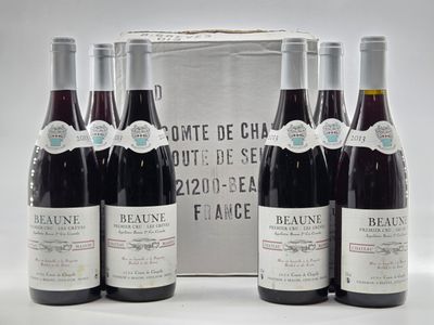 six bottles of red wine sit in front of a silver box