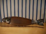 a metal fish on a wooden board on a table