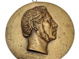 une image représentant un médaillon en bronze orné du visage d'un homme