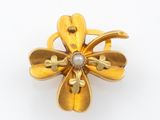 une photo d'une broche en forme de fleur en or, ornée d'une perle au centre
