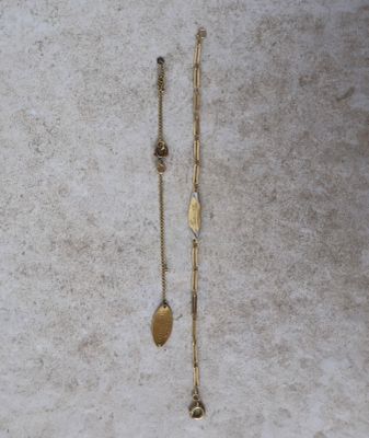un gros plan sur une paire de colliers en or posés sur une surface blanche