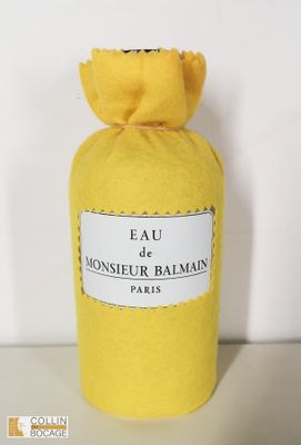 un flacon jaune du parfum « Eau de Monsieur Balmain » posé sur une surface blanche