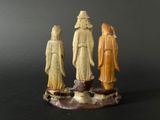 three carved figurines of three people standing on a rock