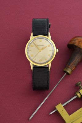 une montre en or et une paire d'outils posés sur un fond rouge