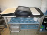 several trays of food are stacked on a metal shelf in a kitchen