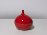 un vase rouge posé sur une table blanche