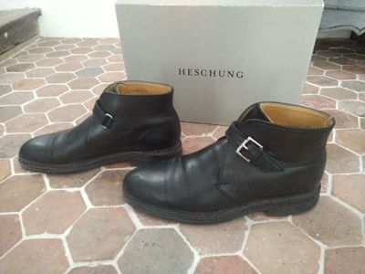 une paire de bottes en cuir noir à boucles posée sur un sol en briques
