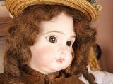 a close up of a doll wearing a hat on a bed