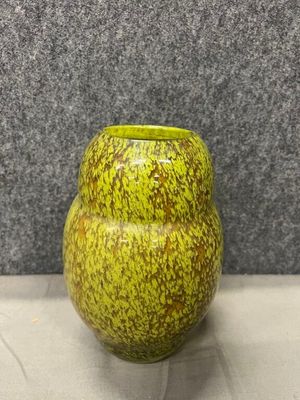 un vase vert posé sur une table, avec un mur gris en arrière-plan