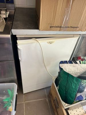 un petit réfrigérateur au milieu d'une cuisine où il y a beaucoup de cartons par terre