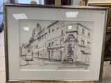 drawing of a building in a frame on a table in front of a window