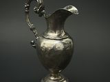 un pichet ancien en argent posé sur un socle, sur fond noir