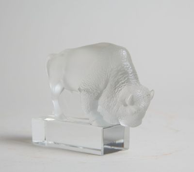 une figurine en verre représentant un bison blanc, posée sur un socle transparent