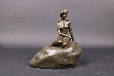 a bronze statue of a woman sitting on a rock
