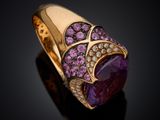 a close up of a ring with a purple stone surrounded by diamonds