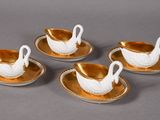 four gold and white porcelain swan cups and saucers on a plate