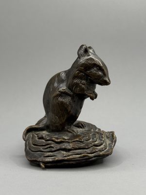 une statue en bronze représentant une souris assise sur un morceau de bois