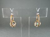 pair of gold tone earrings with green and white stones on clear acrylic stand