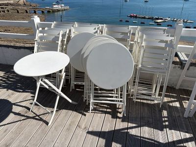 tables and chairs on a deck overlooking a body of water with boats in the distance