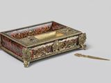 une boîte dorée et rouge posée sur une table à côté d'une paire de ciseaux