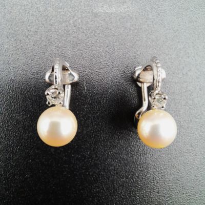 une paire de boucles d'oreilles en perles et diamants posées sur un fond noir