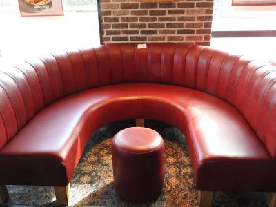 une banquette en cuir rouge avec un pouf rouge devant un mur de briques