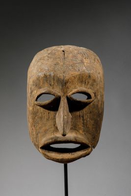un masque en bois posé sur un socle, sur fond gris