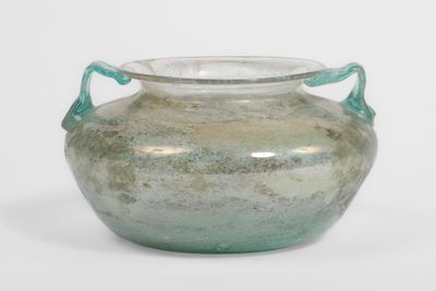 un vase en verre vert muni d'anses, posé sur une surface blanche