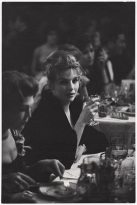 photographie en noir et blanc d'une femme assise à une table avec un verre de vin