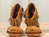 fringed open toe sandals on a wooden table with a curtain in the background