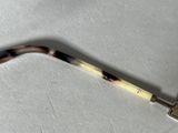 a close up of a metal and tortoise handle on a white surface